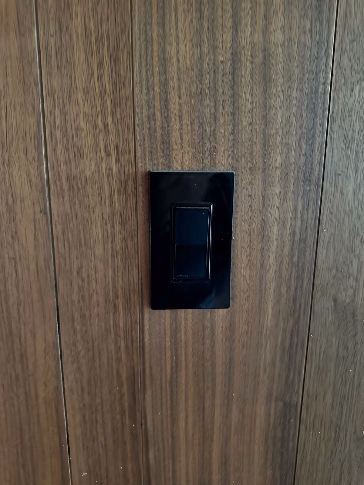 Casa ER - Apagador de diseño en negro, al ras del muro de madera, con la inteligencia Shelly detrás del muro.