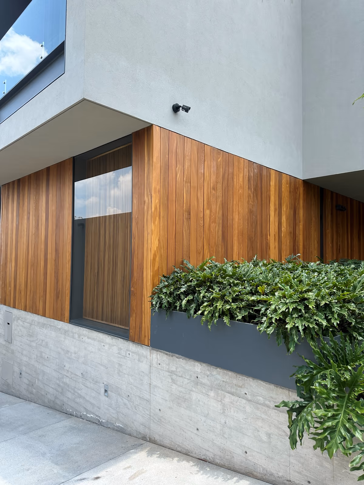 Casa ER - Fachada de concreto, madera y aplanado fino: la cámara bullet Hikvision se integra bajo el alero sin romper la composición.